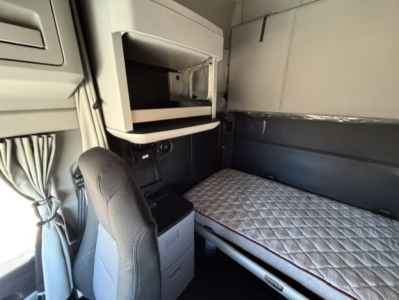 Truck cab interior with sleeper berth in a Kenworth T680 showing a single mattress and overhead storage compartments.