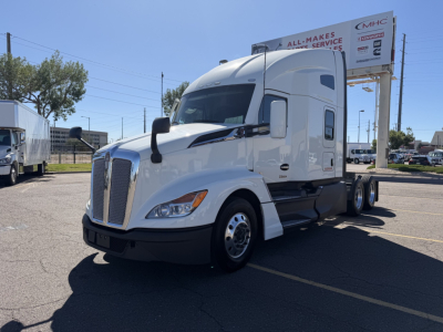 Kenworth T680 tractor-trailer cab in a parking lot with a white exterior. Visible texts include All-Makes Service on the billboard in the background and signage on the truck. No other legible labels clearly readable on components.