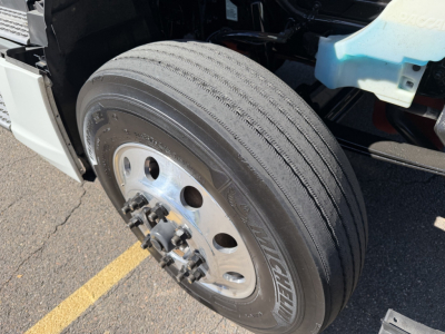 Truck wheel and front suspension area of a 2022 Kenworth T680 showing a dual rear-axle front steer wheel with Michelin tire and alloy wheel, partial cab steps and underside components.