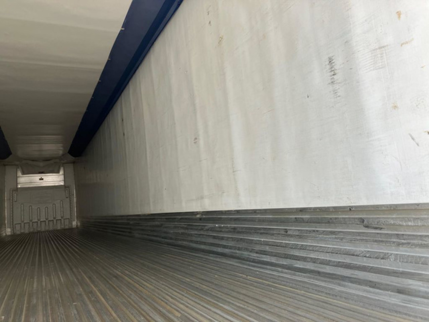 Trailer interior cargo area with metal ribbed floor and aluminum sidewalls, view from rear toward front.