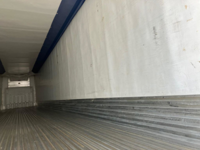 Trailer interior cargo area with metal ribbed floor and aluminum sidewalls, view from rear toward front.
