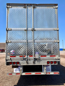 Rear view of a 2017 utility reefer trailer with diamond-plate doors, hinges, and taillights. Various stickers near bottom, and a spare wheel cover on the left.
