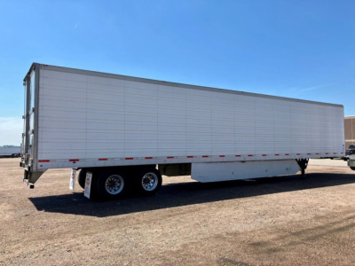 Utility reefer trailer side view showing long white refrigerated box and dual rear axle on a dirt lot.