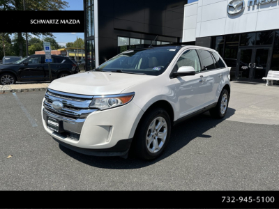 Ford Edge SUV white front three-quarter view showing chrome grille and Ford emblem, dealership lot in background.