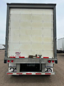 Rear view of a 2016 Wabash van trailer showing a tall vertical white cargo door with metal frame, rear bumper, red brake lights, and bumper reflectors. Visible stickers include a Durapak logo and a small number plate.