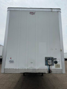 Rear view of a 2016 Wabash van trailer with a white exterior, riveted metal panels, and a small access panel near the lower right with utility connections.