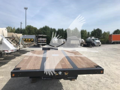 Trailer deck of a lowboy trailer showing wooden planks and black steel frame with lights; front hitch area visible under a clear sky.
