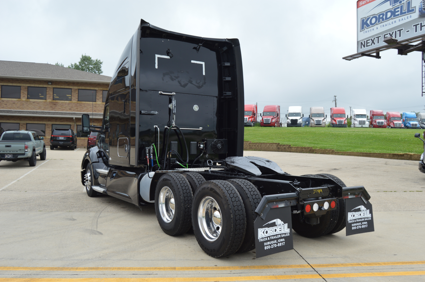 Kenworth T680 tractor rear view showing chassis and dual rear wheels, black paint, aluminum fuel tanks, and rear mud flaps with Kordell Fleet services logo.