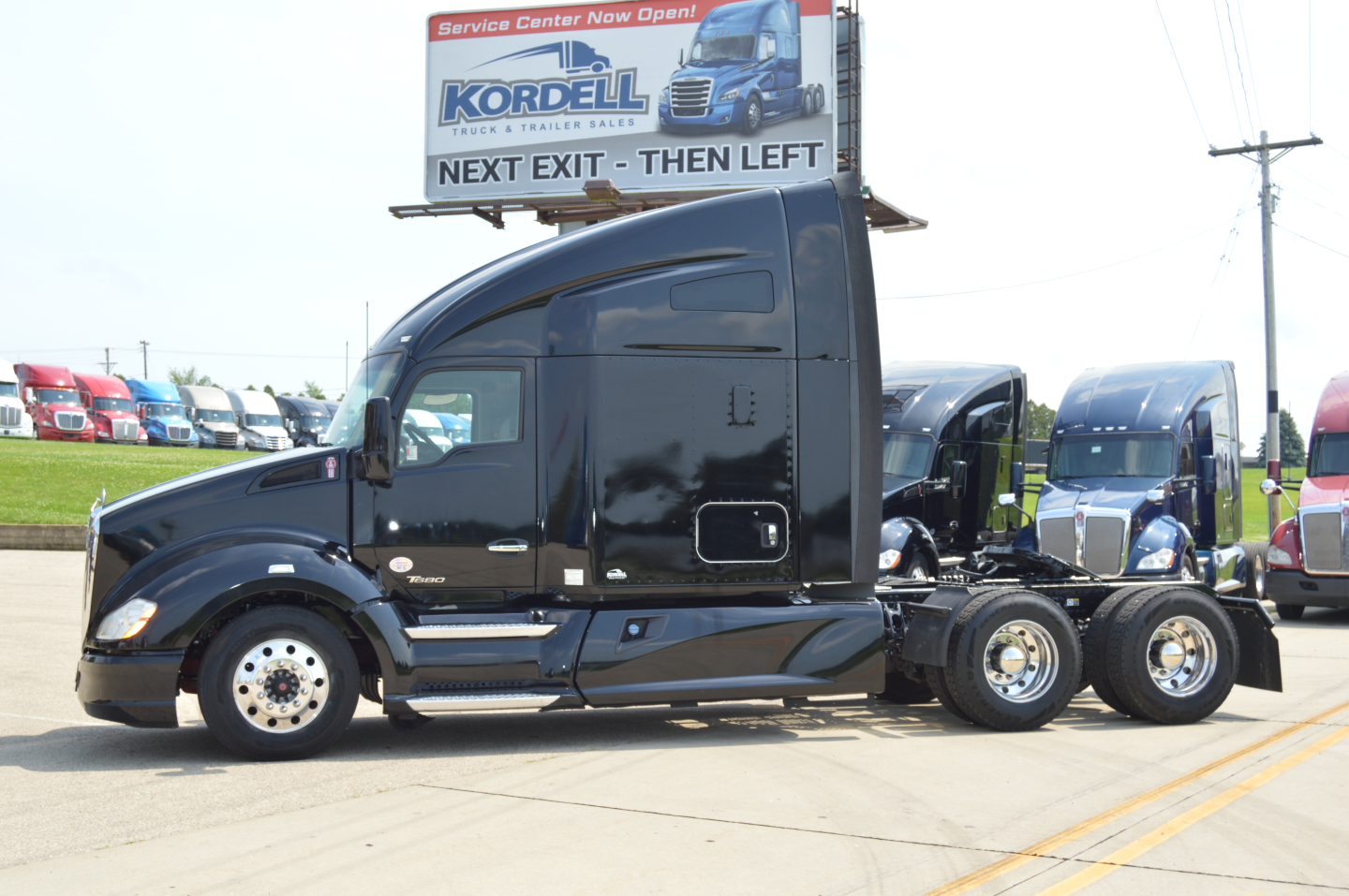 Kenworth T680 tractor unit in service lot showing black exterior and sleeper cab with 3-axle configuration