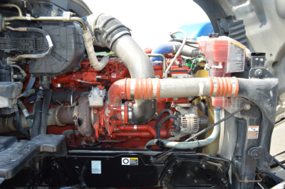 Kenworth T680 engine bay with red engine, coolant reservoir, hoses, and blower; visible components and wiring in a truck engine compartment.