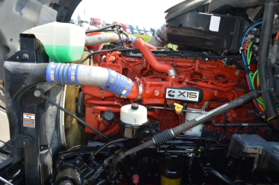Kenworth T680 engine bay showing X15 engine block and blue intake hose with coolant reservoir on left.