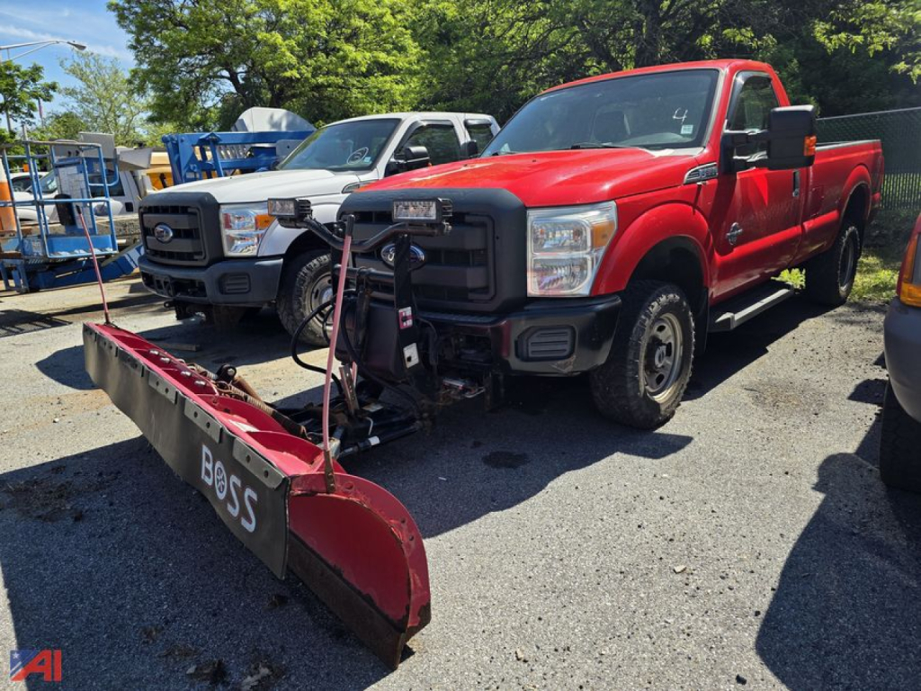 Ford F-350 Super Duty pickup with front plow attached, red crew cab long bed, 4x4, in a used truck lot. Other trucks in background.