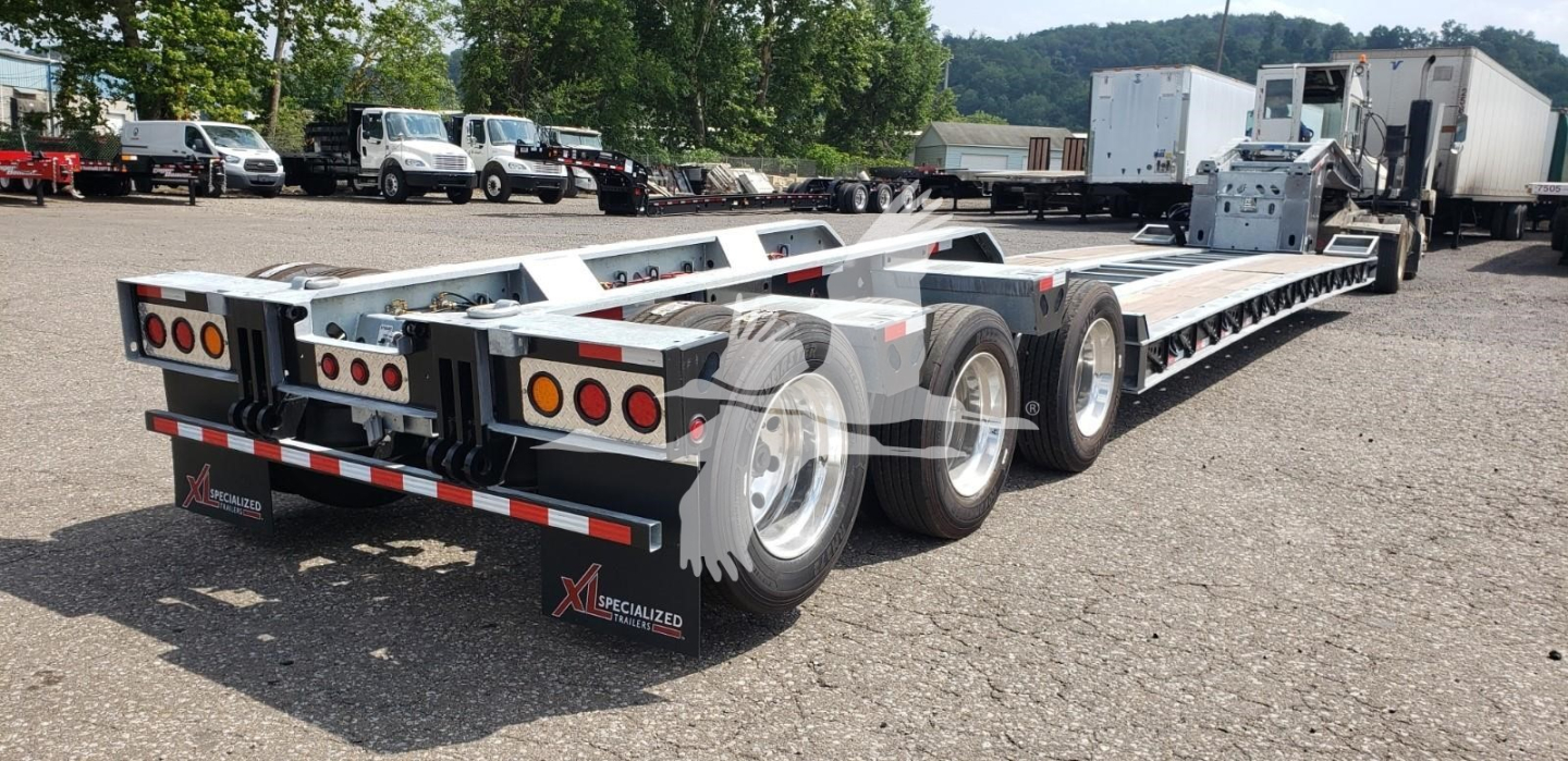 Lowboy trailer with tandem axles and long highway trailer bed, rear view showing dual mud flaps and tail lights, X Specialized branding.