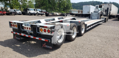 Lowboy trailer with tandem axles and long highway trailer bed, rear view showing dual mud flaps and tail lights, X Specialized branding.
