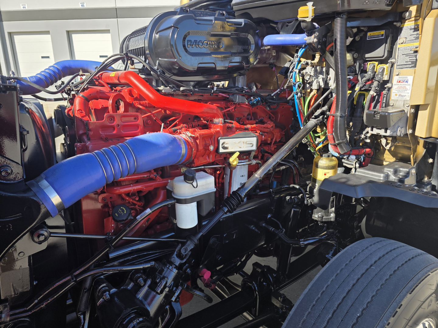 Kenworth T680 engine bay with red engine, blue intake hose, and various wiring and components visible