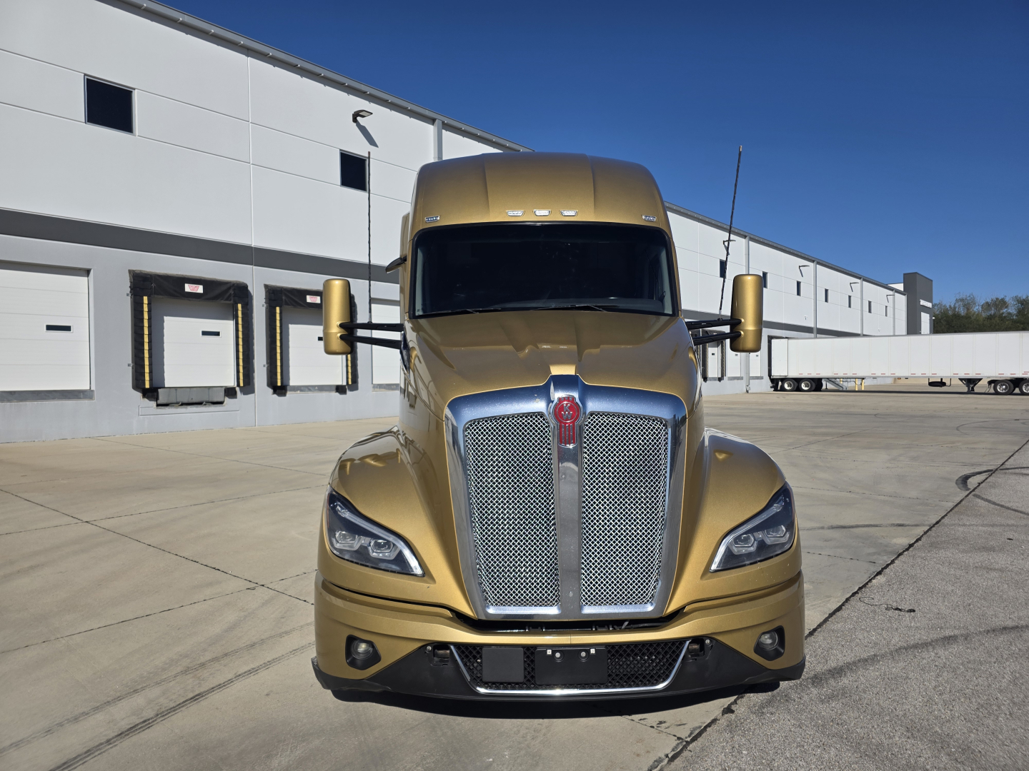 Front view of a gold 2023 Kenworth T680 sleeper cab truck showing chrome grille, headlights, and side mirrors.