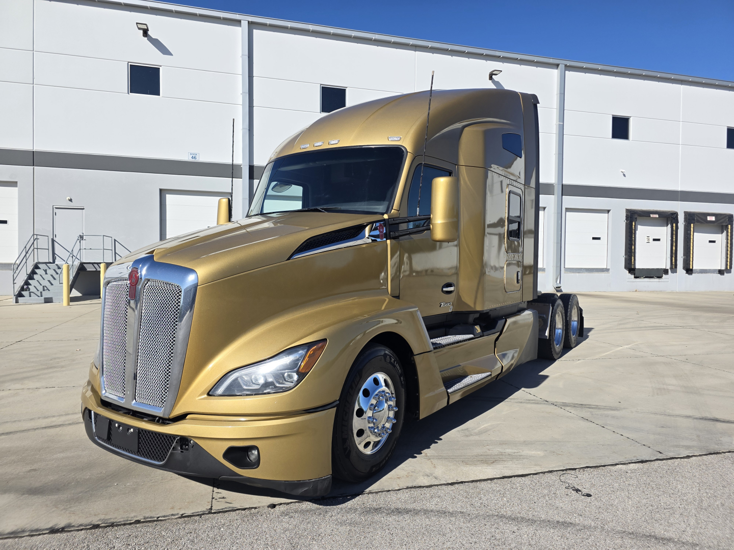 Kenworth T680 sleeper cab truck in gold in a front-side view, showing chrome grille, large headlights, dual rear axles, and a clean factory finish.