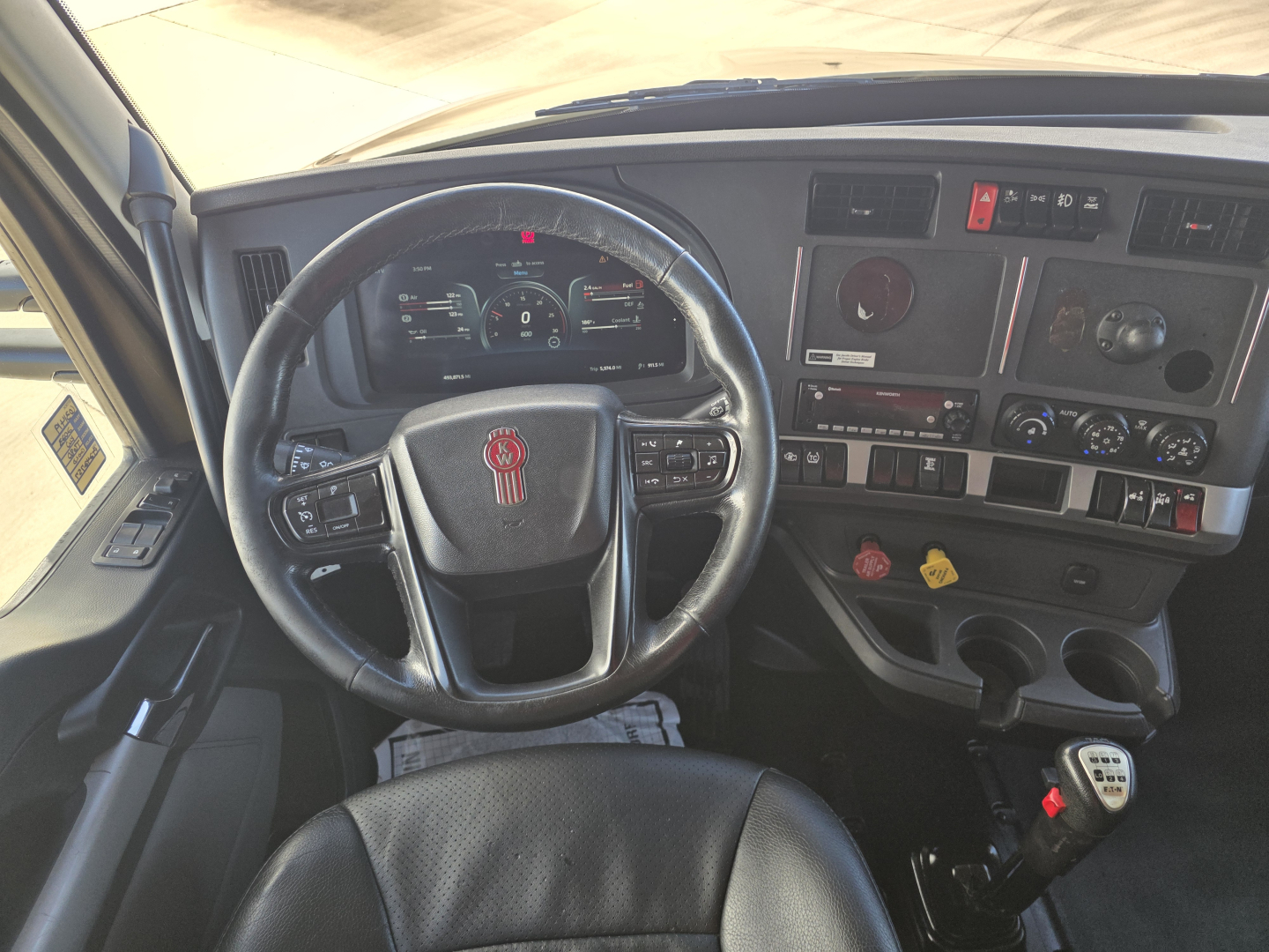 Kenworth T680 interior dashboard with steering wheel, gauges, and control panels. Visible text includes stickers and instrument labels on the dash and center console.