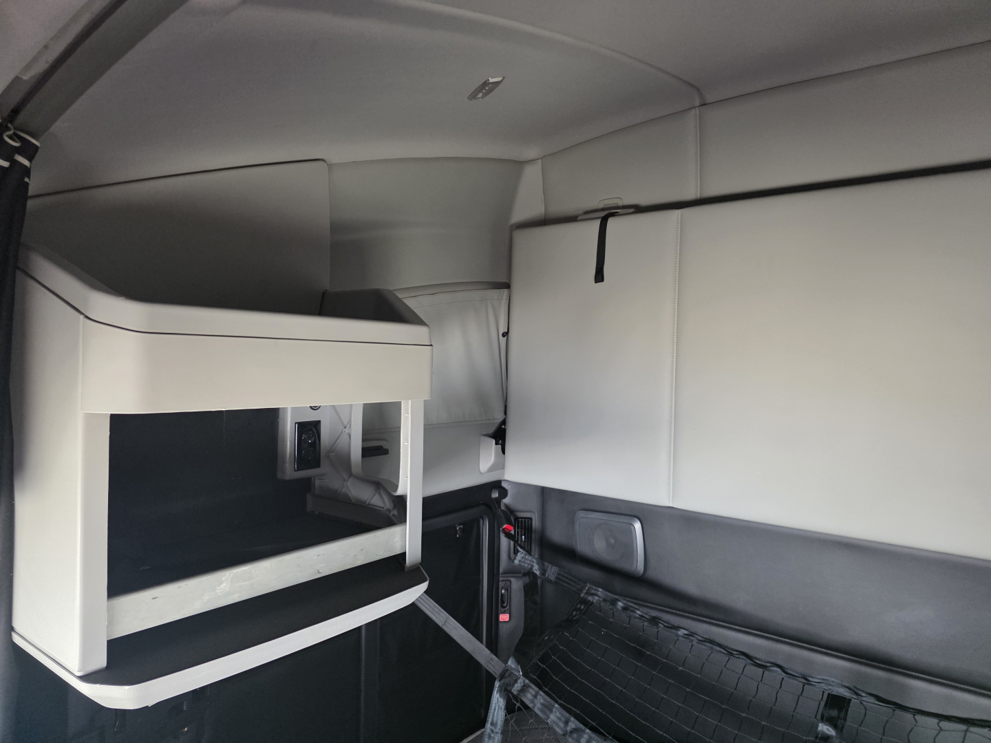 Kenworth T680 sleeper cab interior showing storage cabinet and seating area with light gray panels.