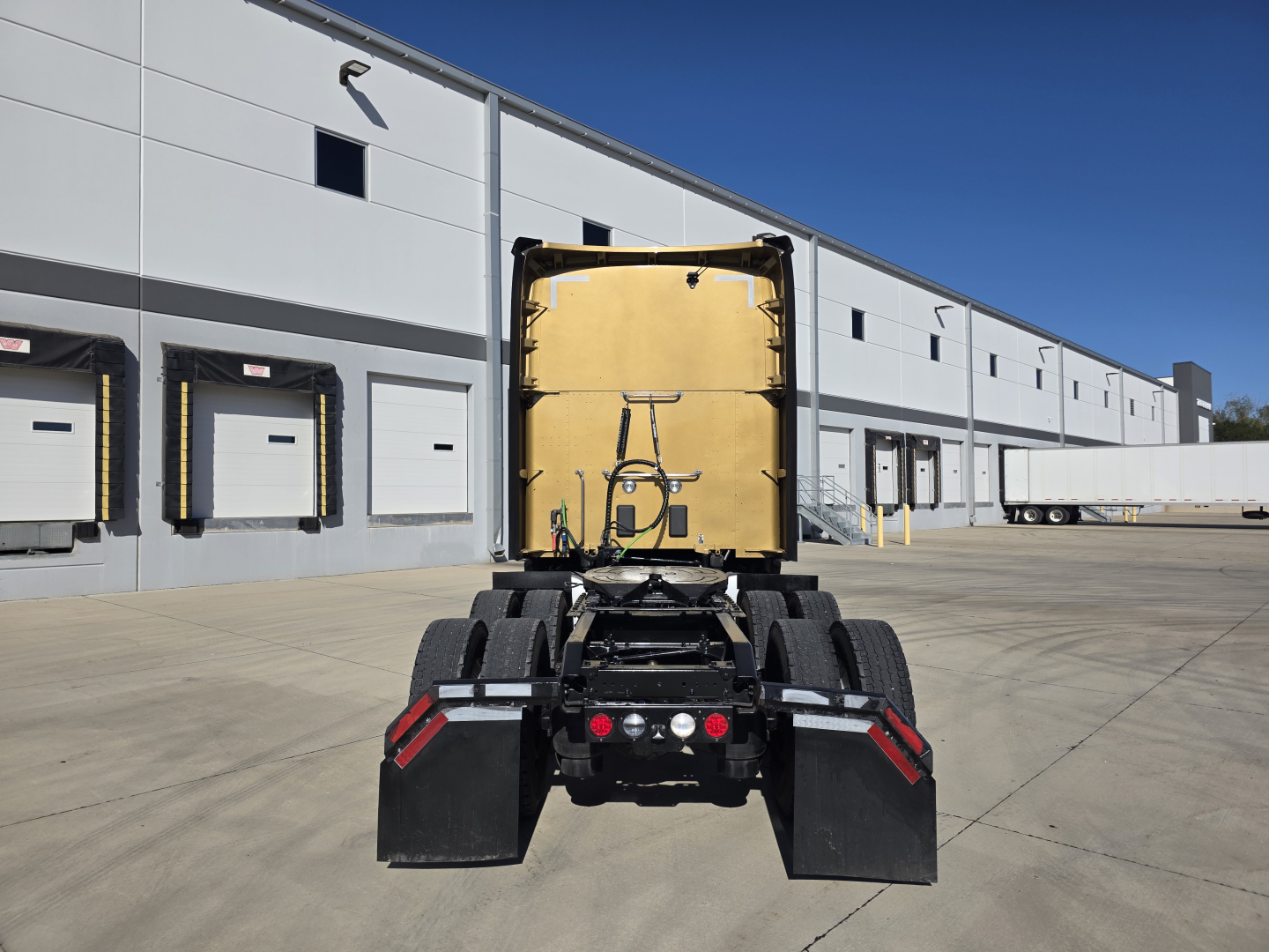 Kenworth T680 tractor rear view showing fifth wheel, dual rear axles, mud flaps, and trailer connection area.