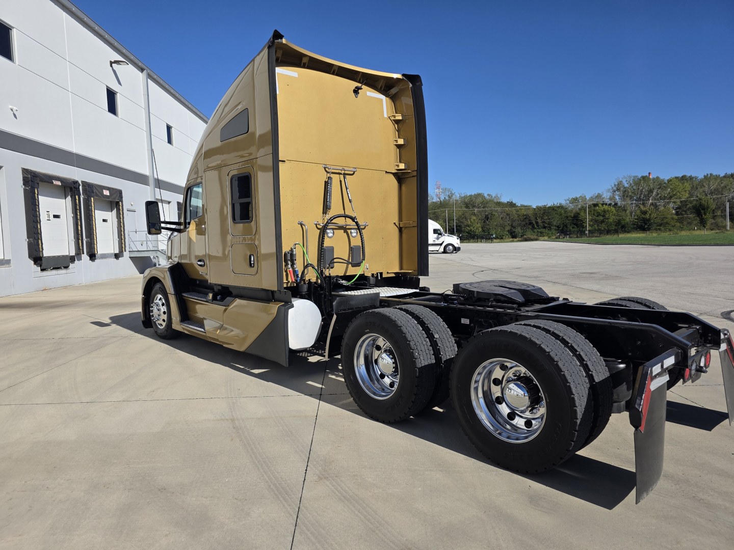 Kenworth T680 sleeper tractor cab rear and chassis showing third axle, fuel tanks, and rear wheels; tan exterior with rear door open area visible.