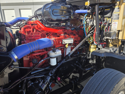 Kenworth T680 engine bay with red engine, blue intake hose, and various wiring and components visible