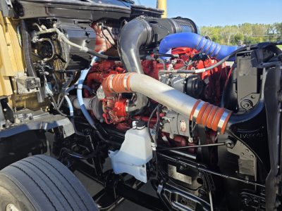 Kenworth T680 engine bay showing large turbocharger and red engine components with blue silicone hose, black frame rails and white coolant reservoir.