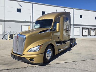 Kenworth T680 sleeper cab truck in gold in a front-side view, showing chrome grille, large headlights, dual rear axles, and a clean factory finish.