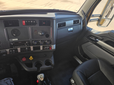 Kenworth T680 dash and driver seat interior showing instrument cluster and controls, manual gear shifter, dual cup holders, and center console