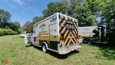 Ambulance rear view with chevron pattern and text 'Ambulance' on the back, side text indicates 'Fire Department' and 'Ambulance' services; another ambulance visible in background