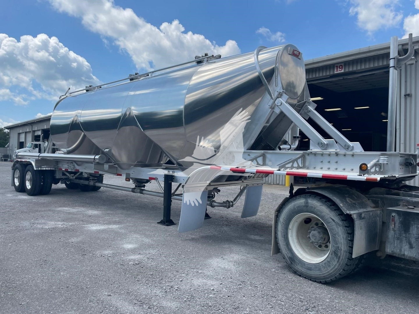 Pneumatic dry bulk trailer shows polished stainless steel Heil Super Jet 1040 with support legs and dual rear axle in a yard.