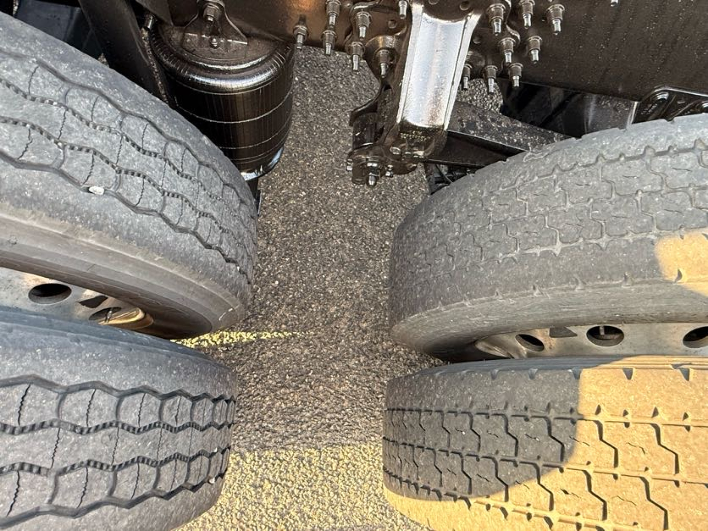 Truck axle area with dual rear tires, suspended undercarriage components, and a black oil filter visible between the wheels.