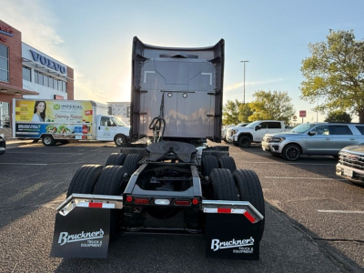 Truck rear view showing fifth wheel and dual rear axles with mud flaps; visible text on mud flaps reads 'Bruckner's TRUCKS EQUIPMENT' and license plate area; surrounding vehicles in lot.
