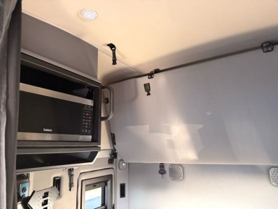 Cab interior showing sleeper truck with overhead storage, microwave, and control panels; Mack AN64T70 cab front visible with light gray interior walls.