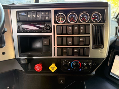 Dashboard of a 2023 Mack AN64T70 showing gauges, switches, and control panels in the driver’s area.