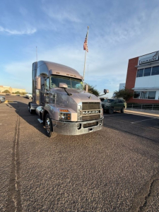 Mack AN64T70 conventional sleeper truck front view in parking lot with flag, showing Mack grille and headlights.