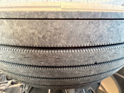 Tire stack in a Mack AN64T70 truck with visible tread and dirt buildup; part of wheel area visible.