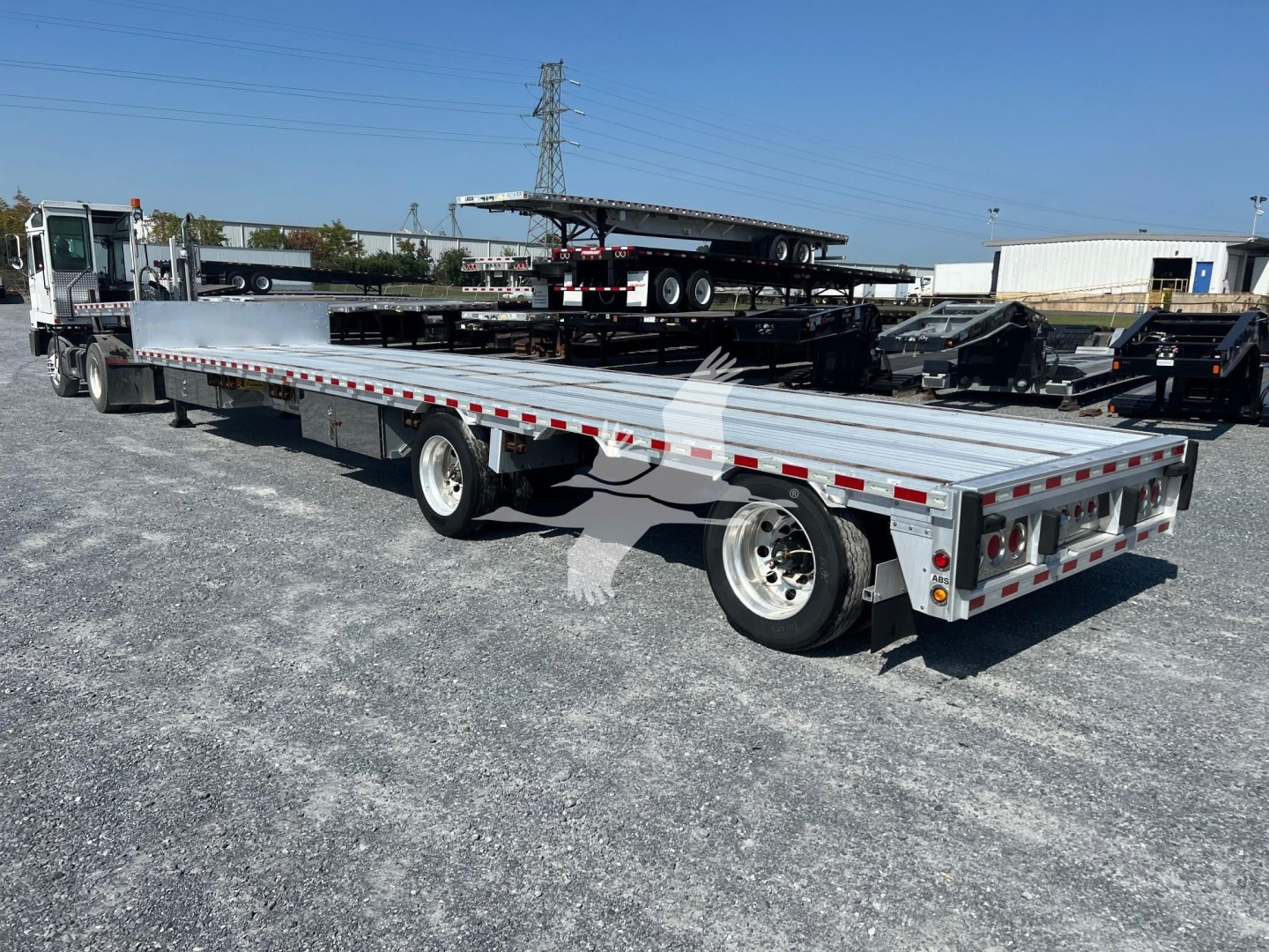 Flatbed trailer showing extended drop deck with multiple axles and rear work lights. trailer bed with reflective tape and dual rear wheels.