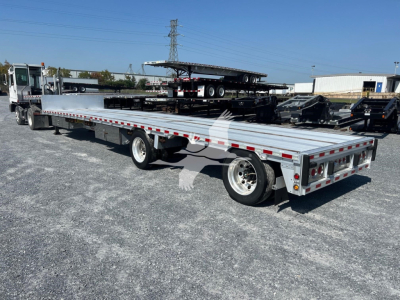 Flatbed trailer showing extended drop deck with multiple axles and rear work lights. trailer bed with reflective tape and dual rear wheels.