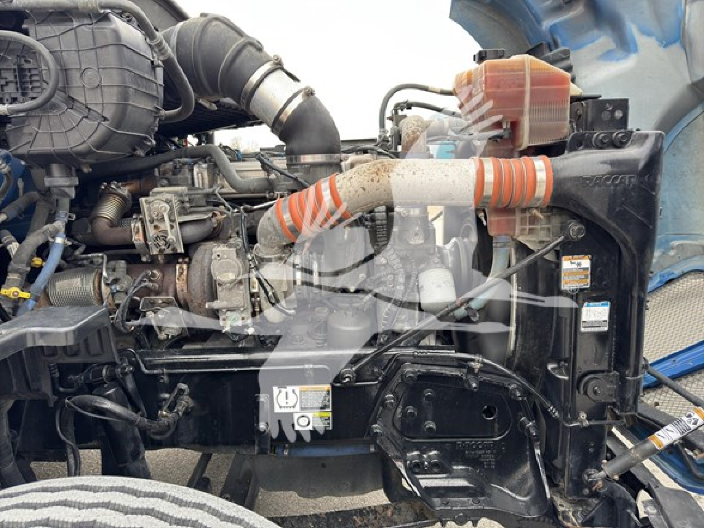 Kenworth T680 engine bay showing turbocharger hose, coolant reservoir, and various engine components with wiring and hoses visible.