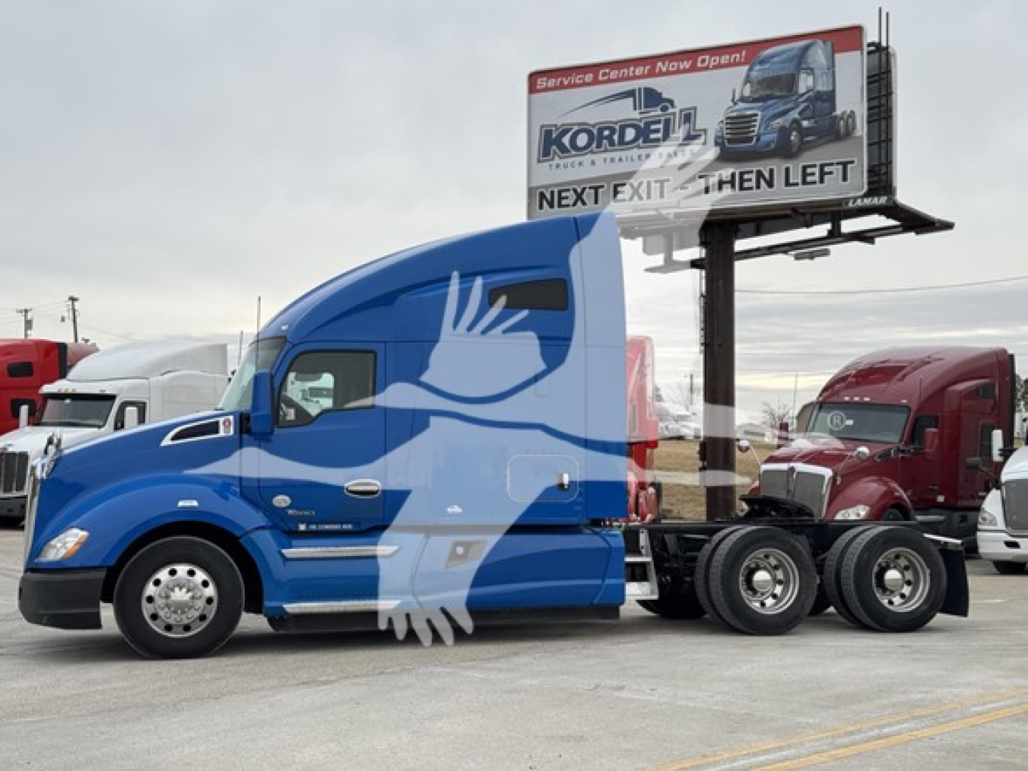 Kenworth T680 truck side view showing blue cab and trailer, with a billboard in background.