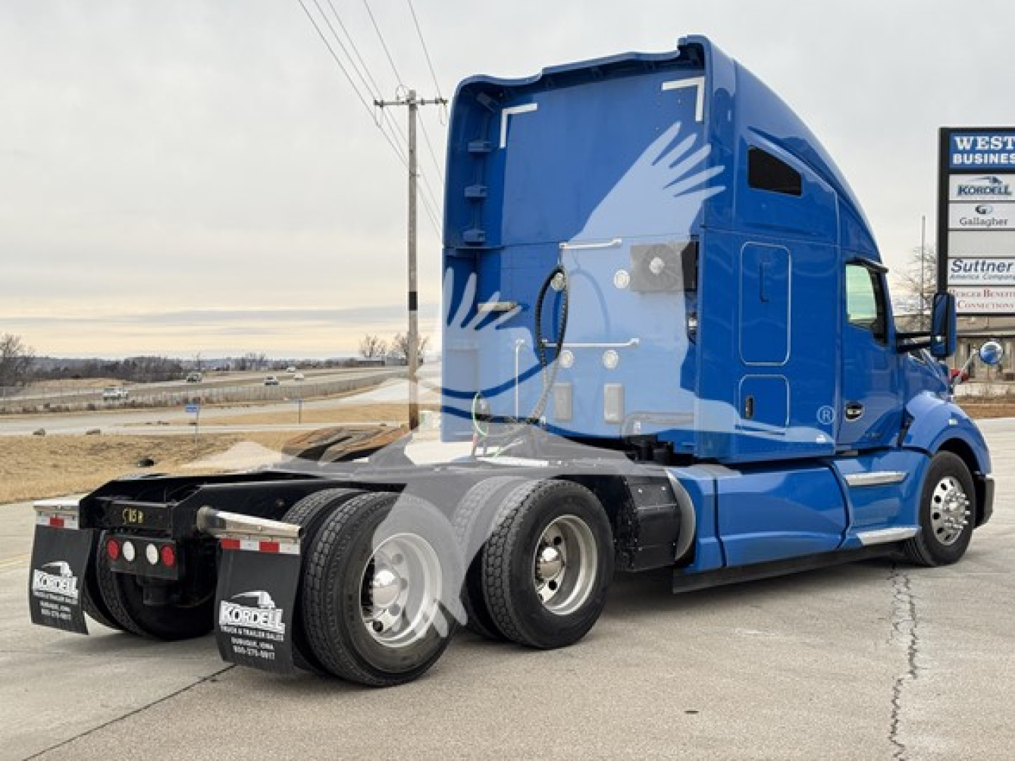 Kenworth T680 tractor in blue sleeper cab, side view showing rear wheels and APUs area.