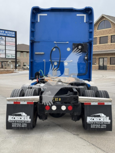 Kenworth T680 rear view showing cargo area interior and back of sleeper, with dual rear wheels, mudflaps, and bumper; visible hoses and components in the open truck bed.