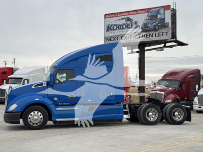 Kenworth T680 truck side view showing blue cab and trailer, with a billboard in background.