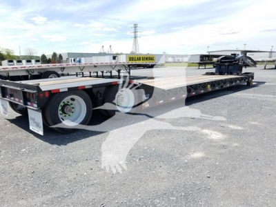 Lowboy trailer showing twin axles and metal deck with reflective tape and DOT tires.