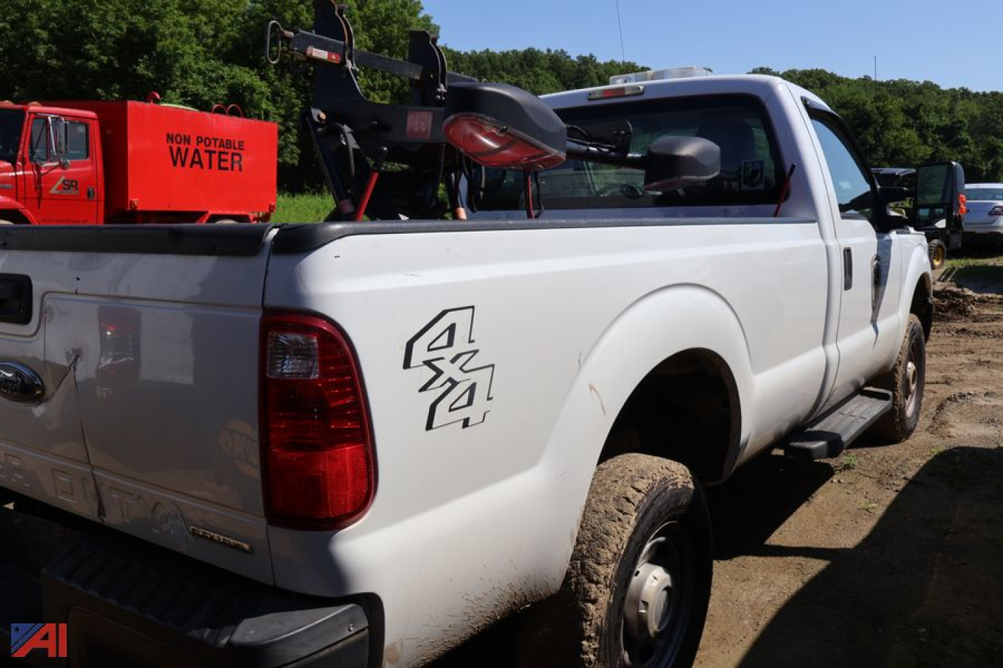 Ford F-250 Super Duty pickup truck with plow; side rear quarter shows 4x4 decal and mud on tires; white truck, red non-potable water tank in background.