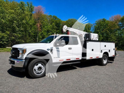 Ford F-550 service/utility truck with bucket lift, white, side view. VIN tag not visible on image. The truck has a utility body with compartments along the bed and a bucket lift mounted on rear.