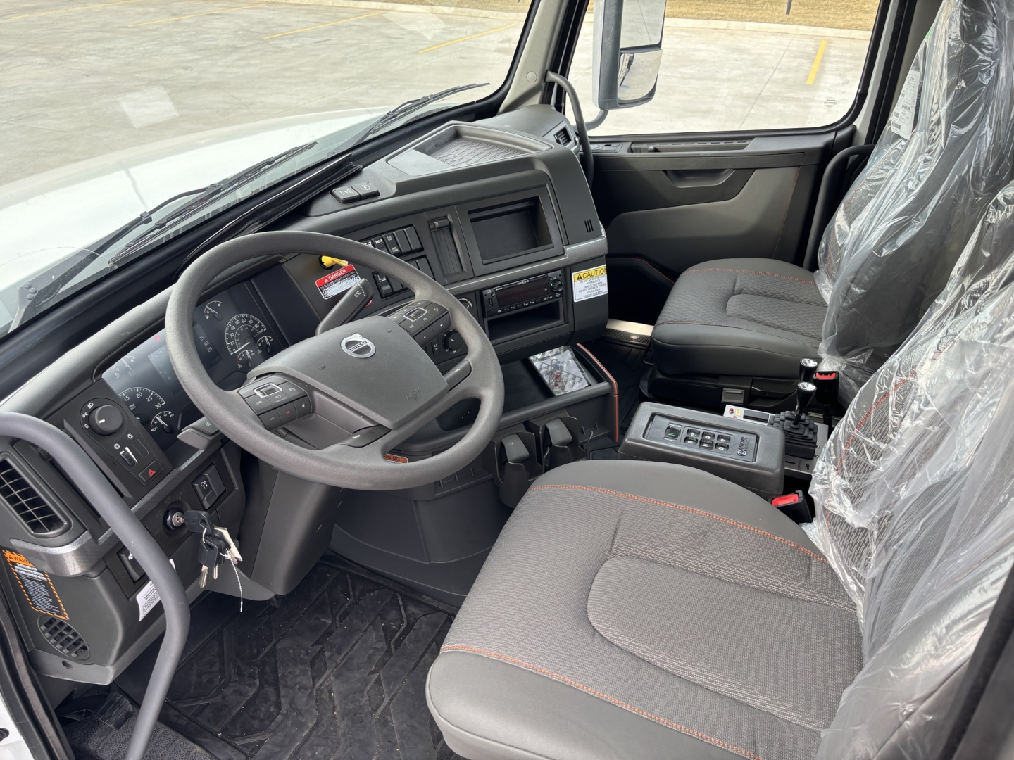 Volvo VHD64B300 cab interior showing steering wheel, dashboard, and central console with seats and plastic seating covers.
