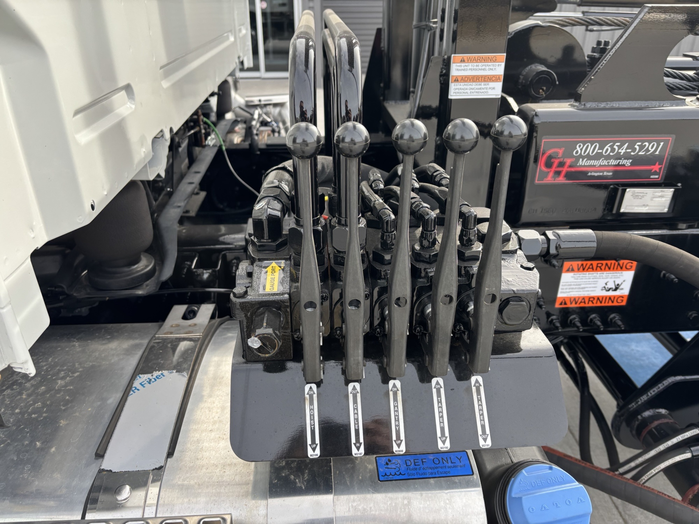 Volvo VHD64B300 roll-off truck control levers and hydraulic valve block with labels and warning stickers visible.