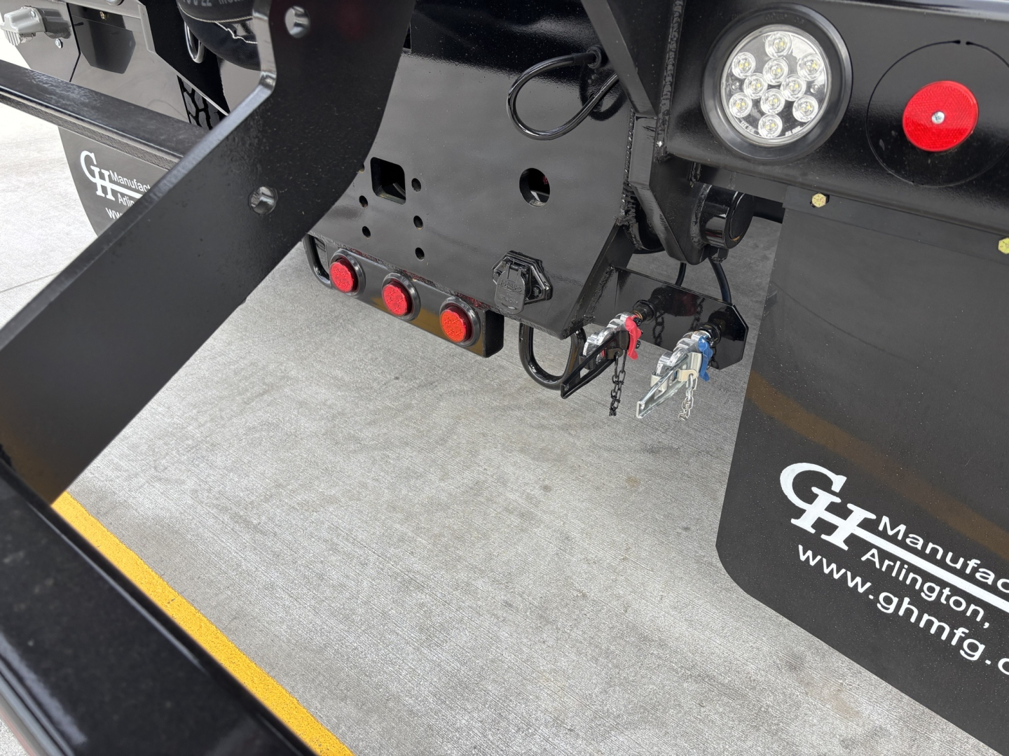 Front hitch area of a new Volvo VHD64B300 rolloff truck showing hydraulic lines and wiring, circular marker lights, and GV logo plate.